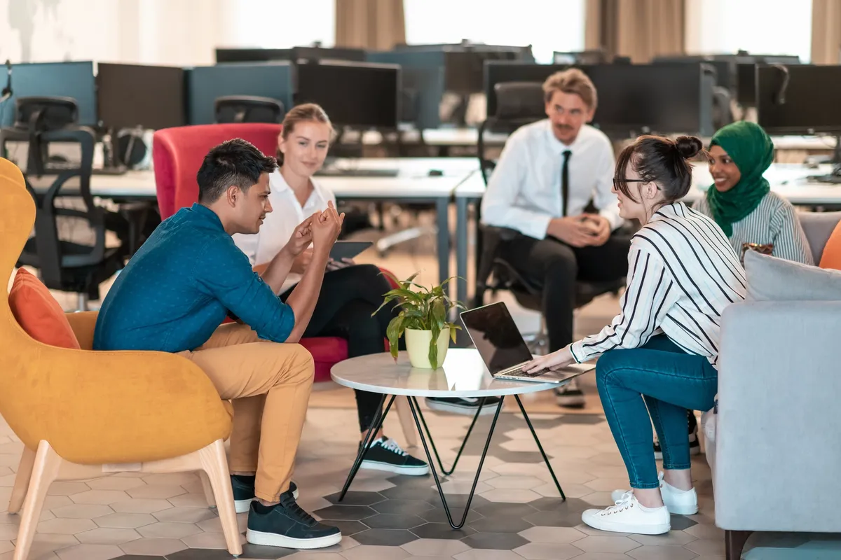 Multiethnic startup business team having brainstorming in relaxation area of modern office interior working on laptop and tablet computer. High-quality photo