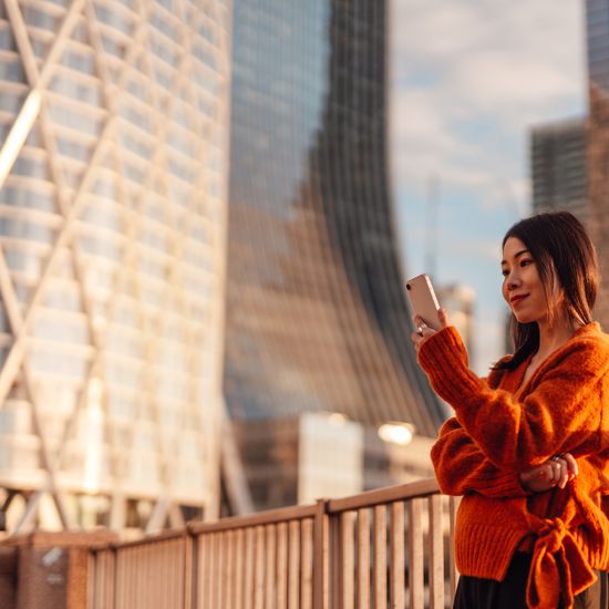 Young Asian businesswoman using mobile phone in financial district at sunset. Lifestyle and technology. Concept of career achievement and investment planning.Colorful Human