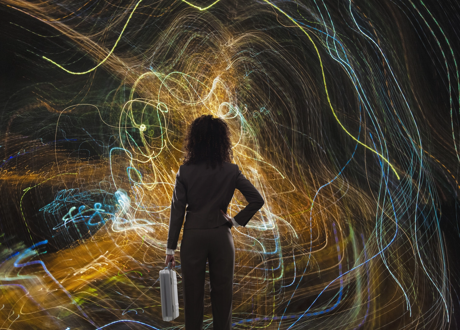 A woman executive faces a chaotic tangle of data in the form of light trails in an image about leadership, technology and big data.