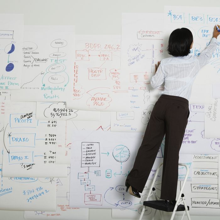 Businesswoman standing on step ladder writing on flow chart