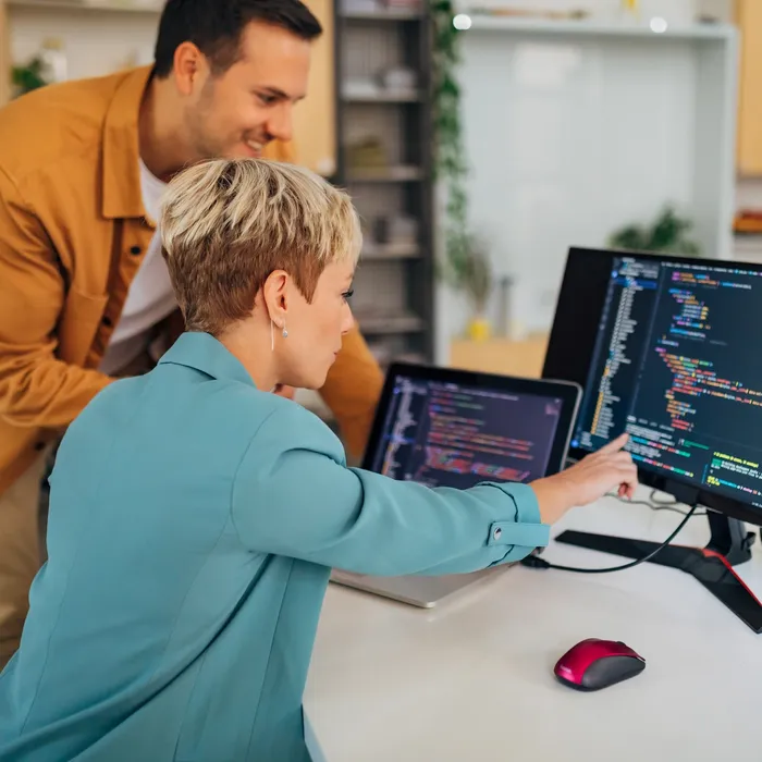 A female programmer listens carefully to her male colleague programmer who explains to her how to code a program