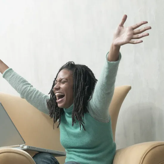 Young woman, sitting in armchair with laptop, arms outstretched
