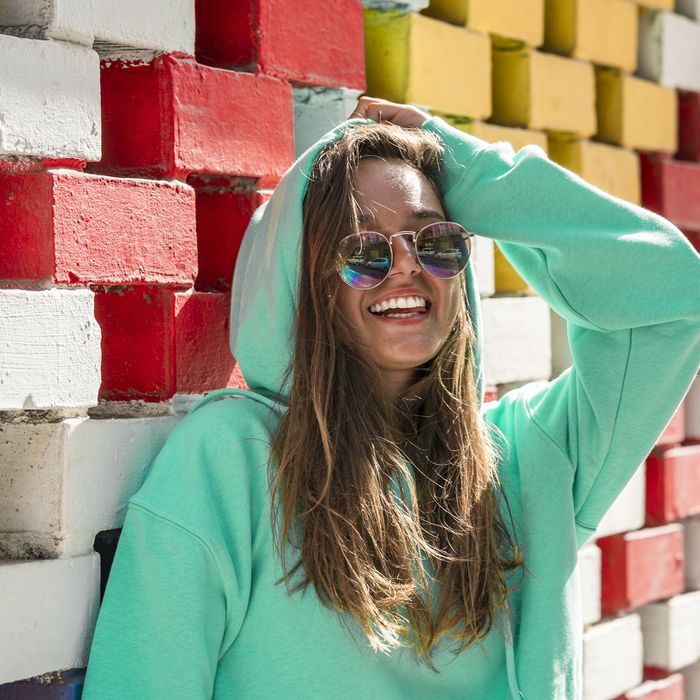 Smiling woman with hand in hair standing against brick wall