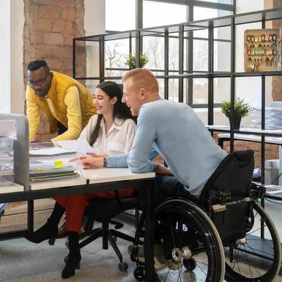 Three people around a work desk; one is in a wheelchair