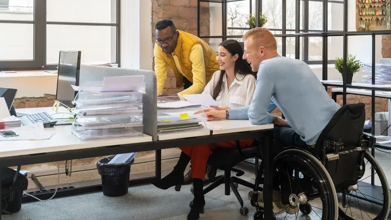 Three people around a work desk; one is in a wheelchair
