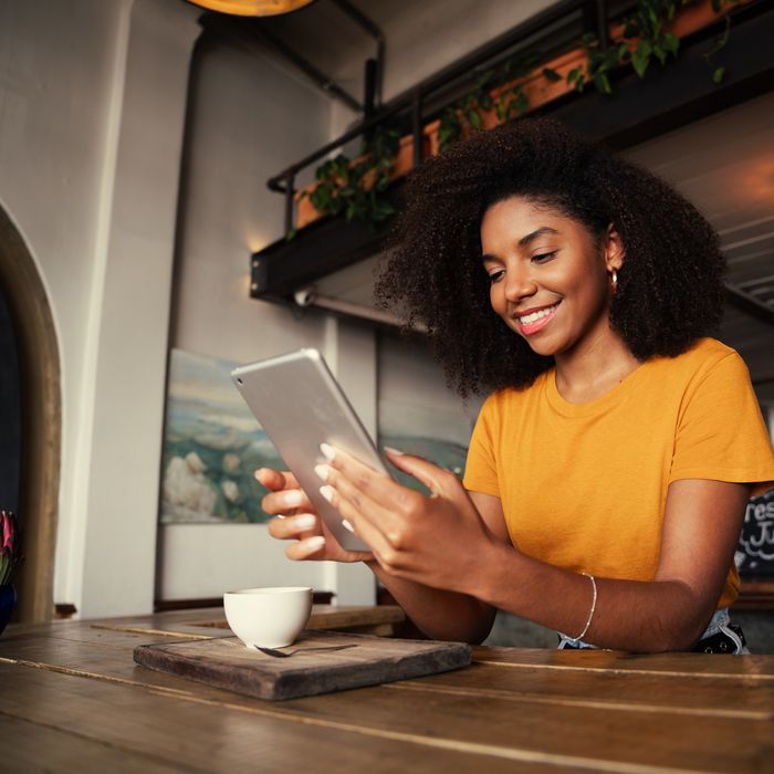 Low angle shot of unique African American woman searching on digital tablet sitting at funky tearoom with hot latte. High quality photo