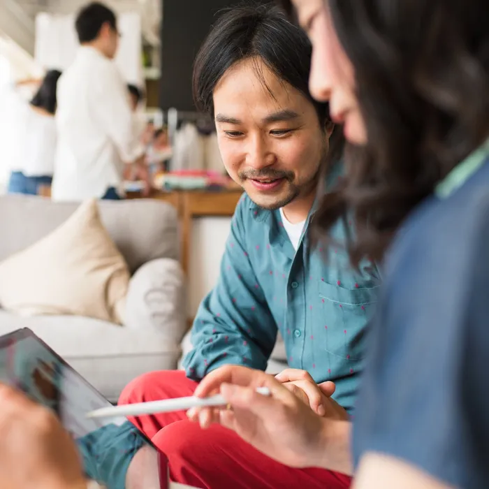 Two coworkers in casual clothes having a business meeting and looking at data on a digital tablet. Kyoto, Japan. May 2016