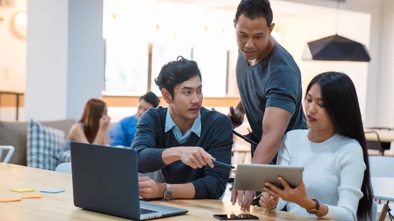 Young design team in a modern looking office having an informal meeting and looking at information on a digital tablet. Bangkok, Thailand. April 2017