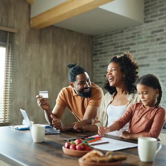 Happy African American parents shopping online view laptop at home while their daughter is drawing.