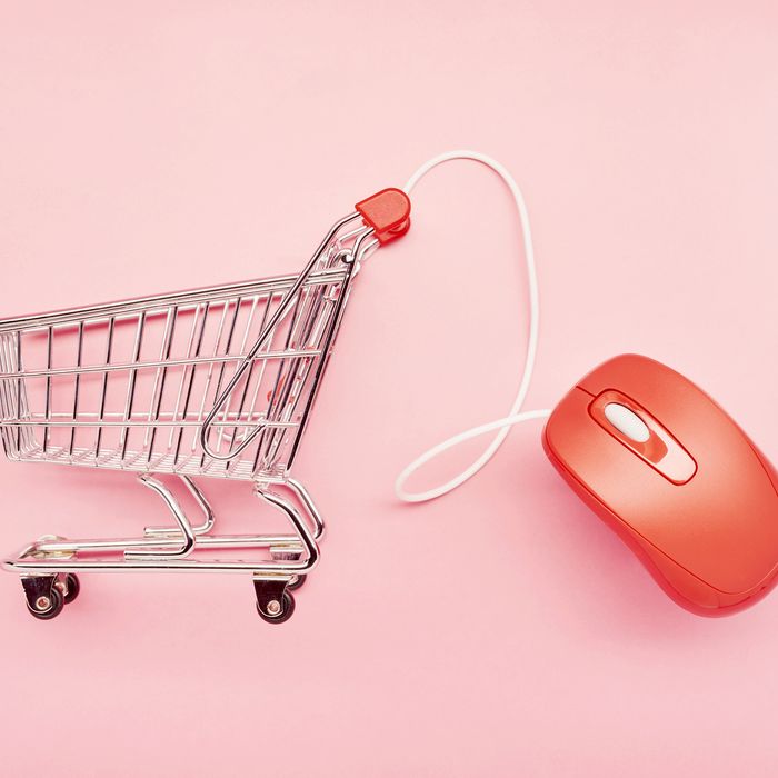 Still life of a small shopping cart and red computer mouse on pink background, online shopping