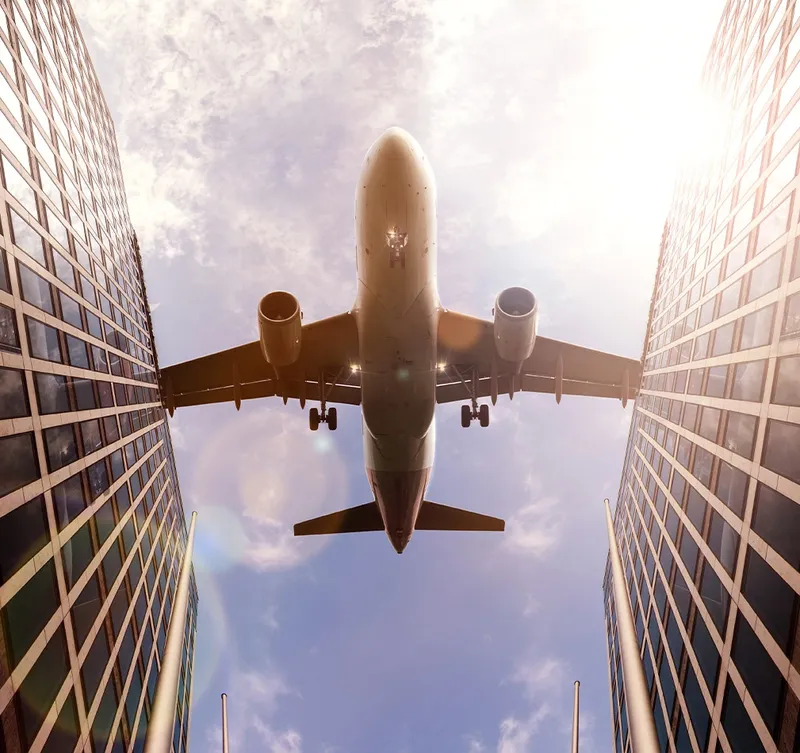 View from below of plane flying between skyscrapers