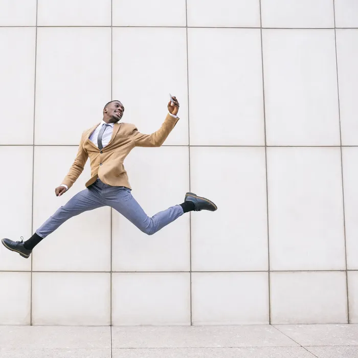 Young businessman jumping and taking a selfie in front of a wall