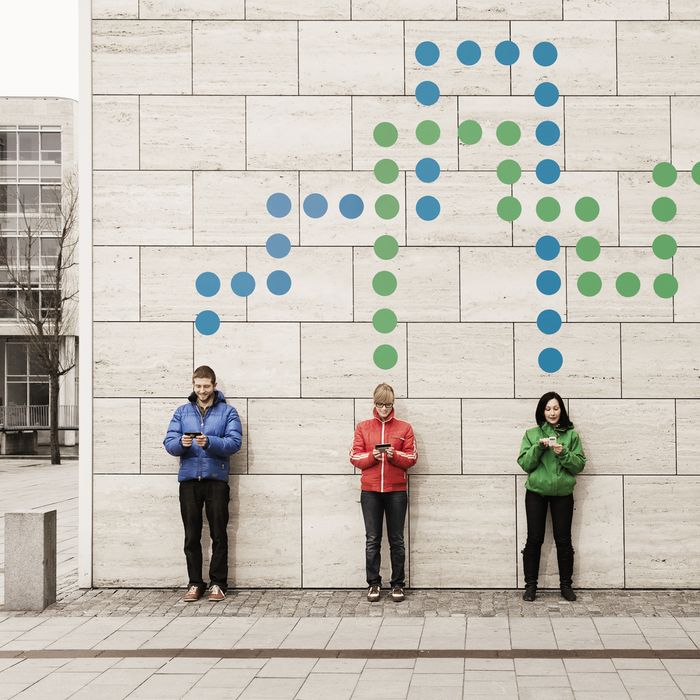 A group of young people standing against a wall using their mobile phones. They are connected with dots.